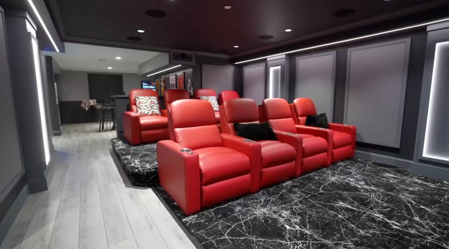 Home theater with two rows of bright red leather recliners, black marble floor, gray acoustic paneling.