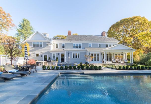 Elegant backyard with a pool, patio furniture, and a large, beautiful house in the background.