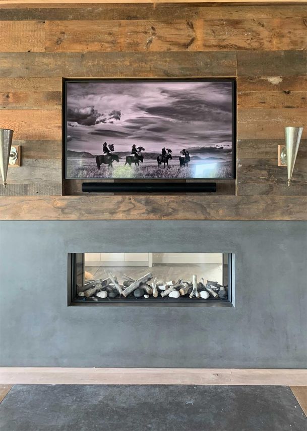 Rustic living room with a wooden accent wall, a TV, and a double-sided fireplace.