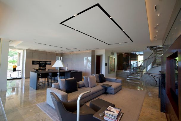 A spacious open-plan living area with a gray sofa, modern kitchen, and a spiral staircase, featuring marble flooring and sleek design elements.