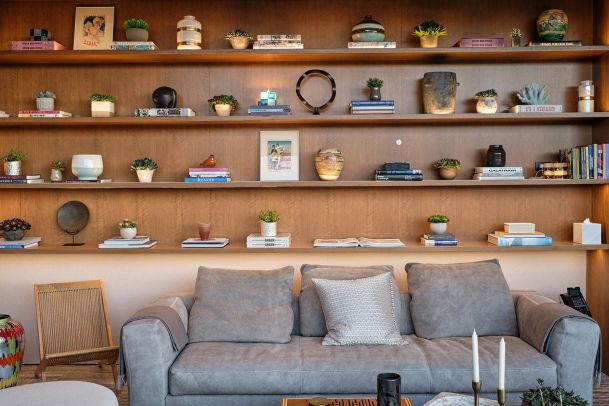 A stylish living room with a gray sofa, wooden shelving filled with decorative items and books, and a cozy ambiance.