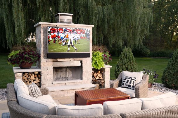 Outdoor patio with a stone fireplace, Seura Waterproof TV, and comfortable seating.